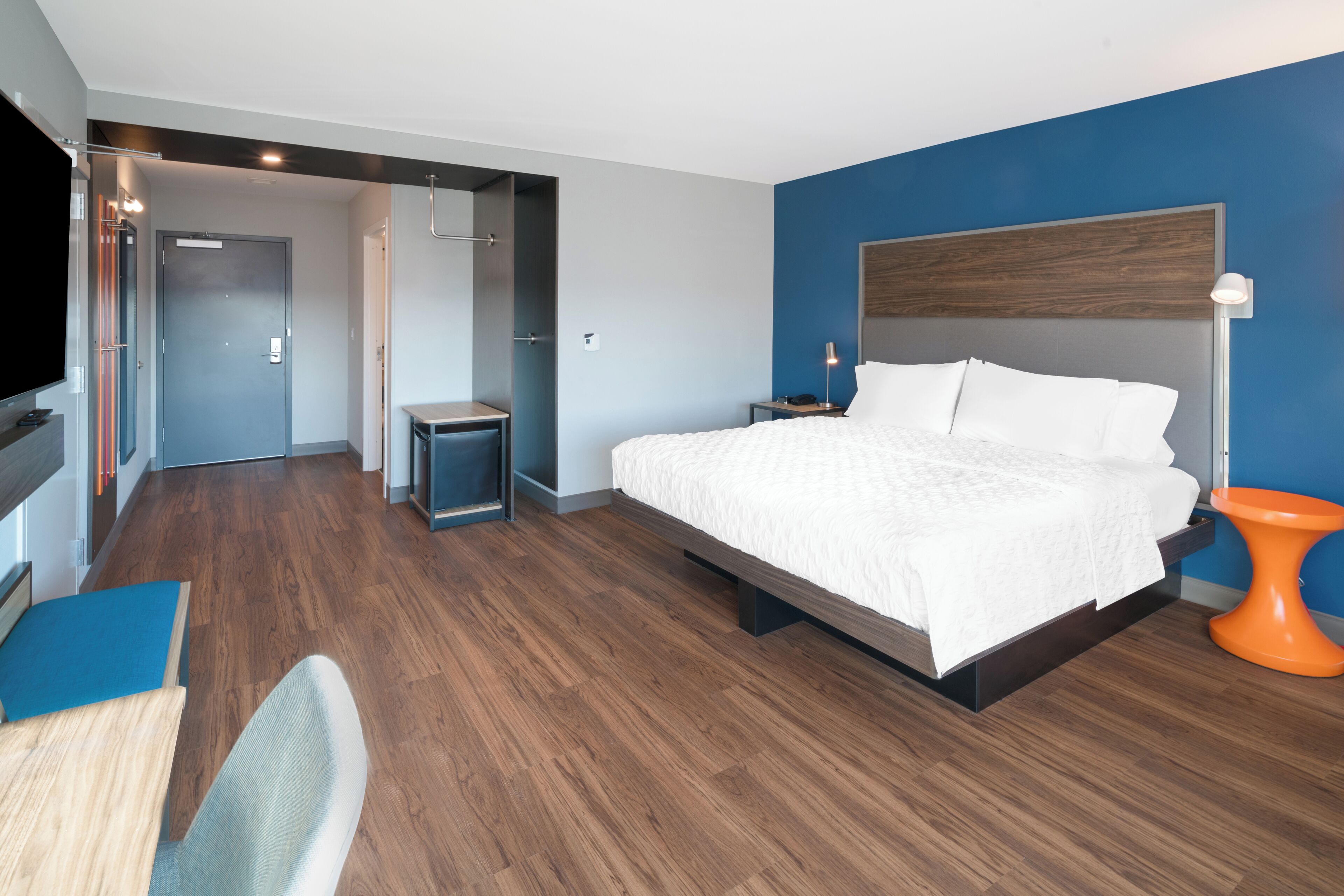 Una habitación de hotel moderna con una cama grande, un escritorio con una silla, un televisor y un baño con ducha e inodoro.