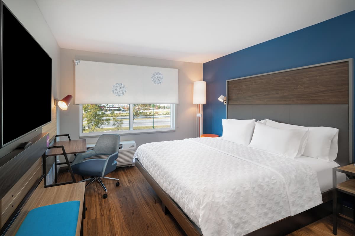 Una habitación de hotel con una cama grande, un escritorio con una silla, un televisor de pantalla plana y una ventana con persianas.