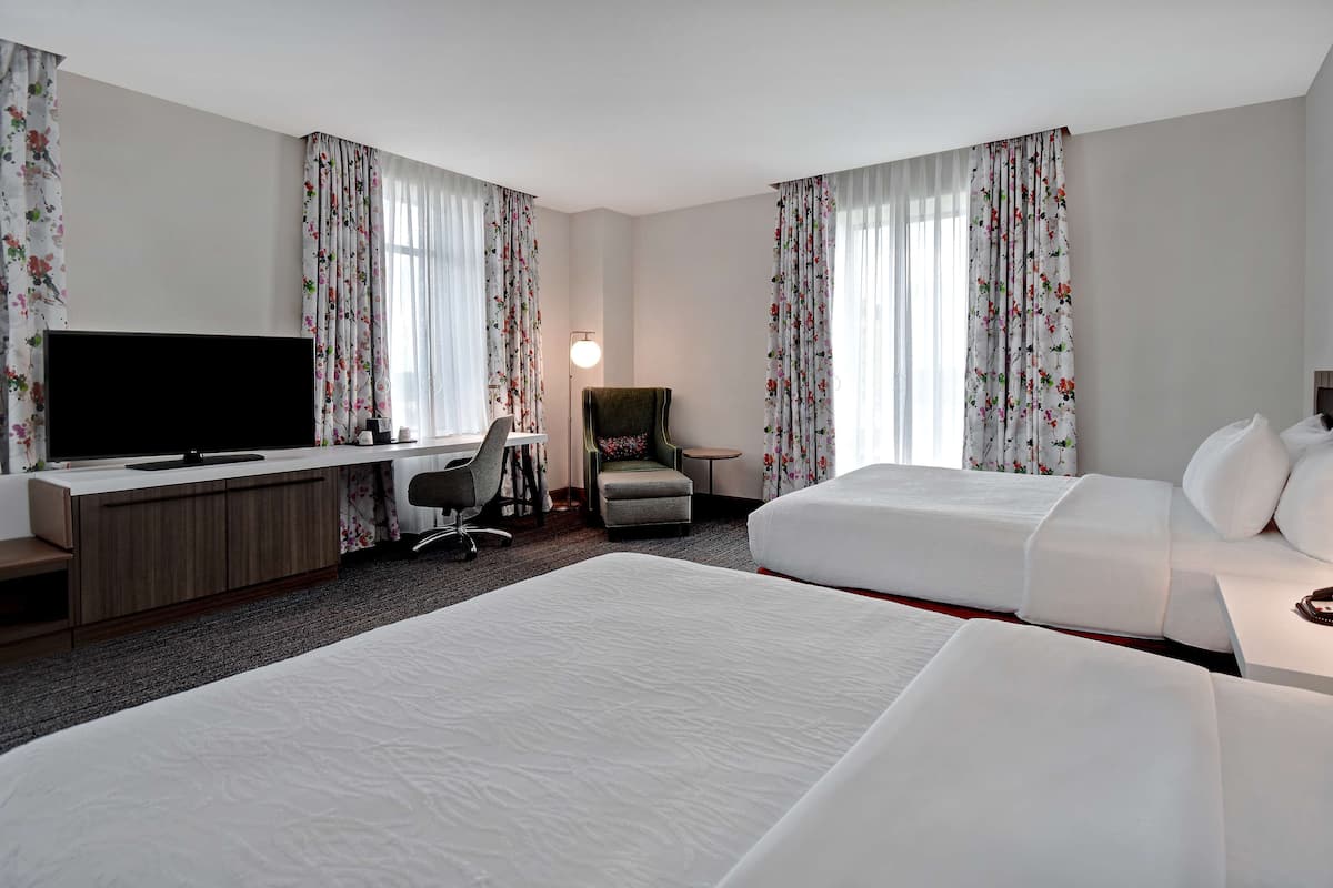A hotel room with two beds, a desk with a TV, a chair, and a lamp.