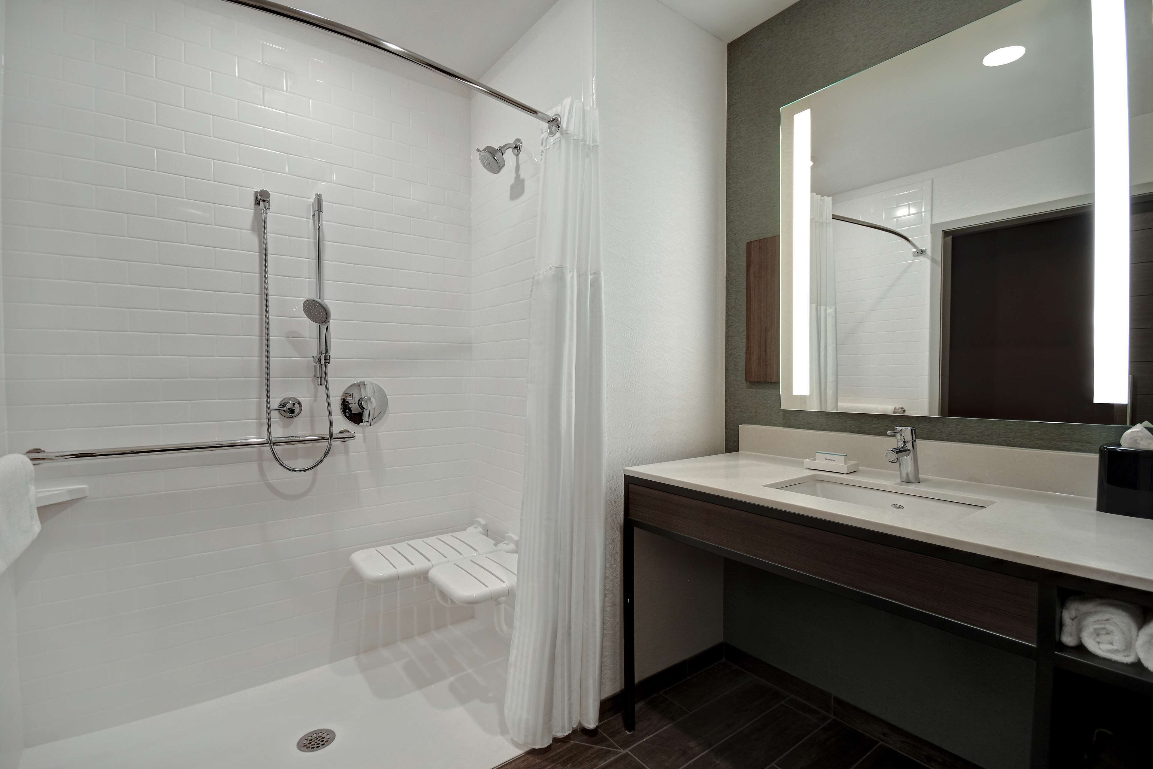 Un baño moderno con ducha a nivel, un espejo grande y un tocador con lavabo.