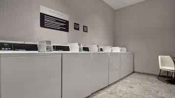 A laundry facility with multiple washing machines and dryers, a sign indicating guest laundry use, and a white chair.