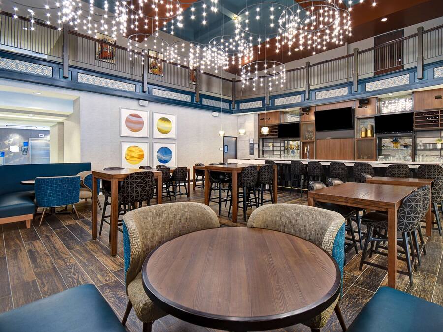 Un restaurante espacioso con techos altos, luces colgantes y diversas opciones de asientos, incluyendo mesas redondas y cabinas.