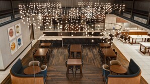 Ein modernes Restaurant mit verschiedenen Sitzbereichen, darunter runde Tische und Sofas, sowie einer zentralen Bar.