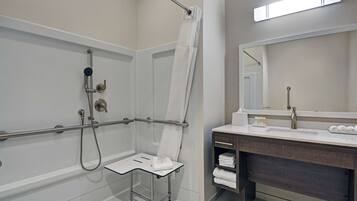 Un baño moderno con ducha, barra de apoyo y tocador con espejo y perchero.