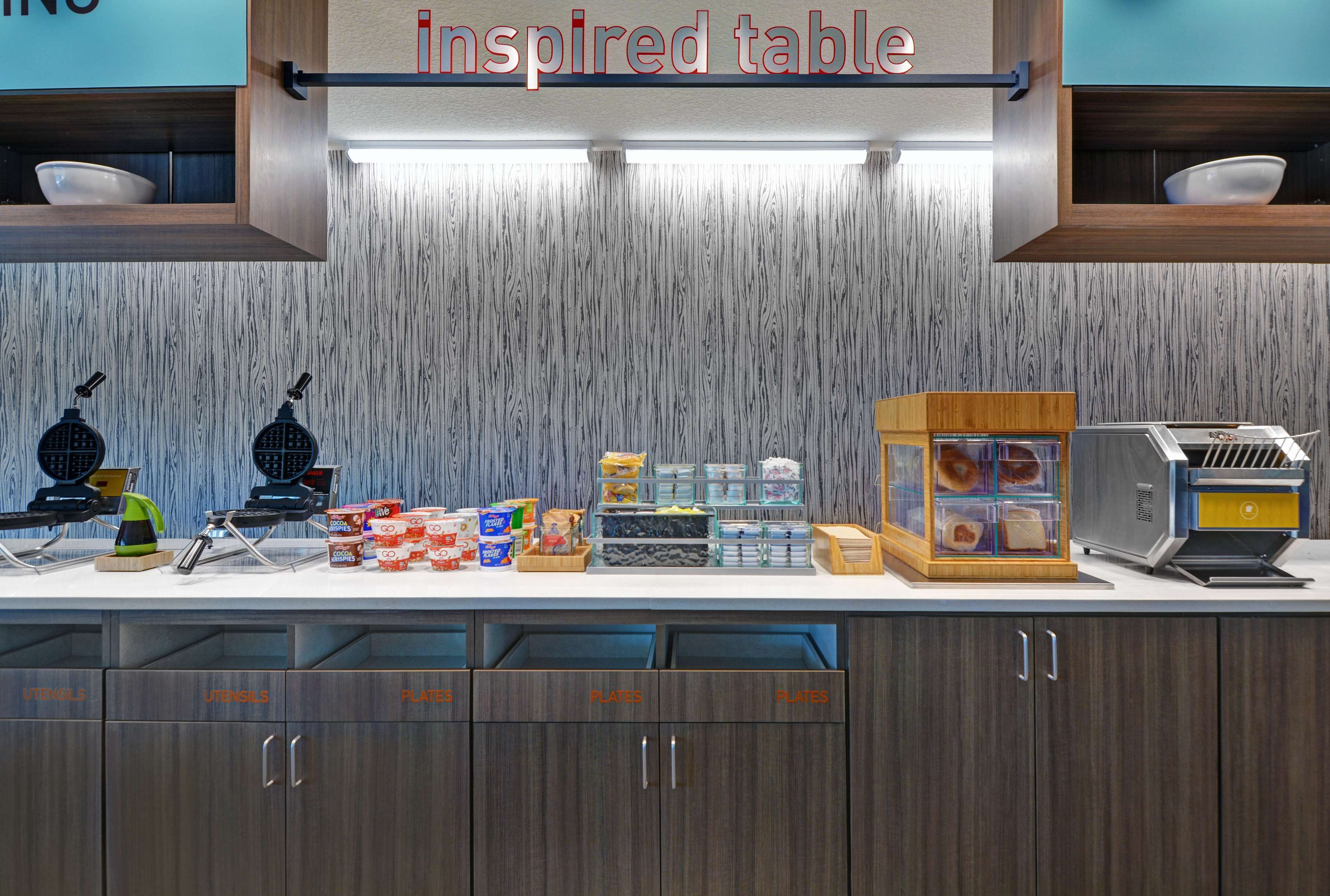 A self-service breakfast area with a variety of food items, utensils, and plates.