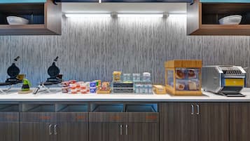 A self-service breakfast area with a variety of food items, utensils, and plates.