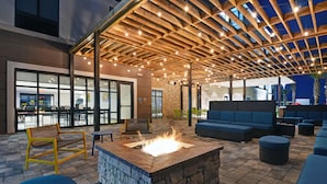 Een terras buiten met vuurkorf, zitplaatsen en een pergola.