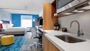 Een moderne hotelkamer met een bed, bureau, stoel en kitchenette.