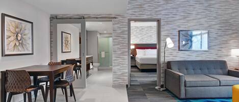 A modern hotel room with a dining area, a sofa, and a bed.