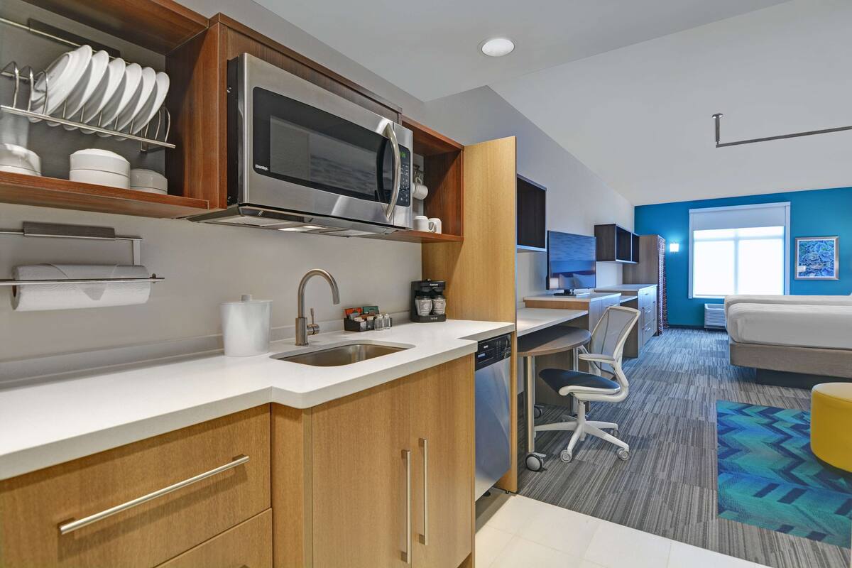 A modern kitchen with a microwave, sink, and cabinets. There is a dining area with a chair and a couch.