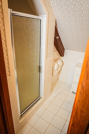 Bathroom features a shower area with a frosted glass door, white tiles, and a towel rack.