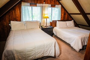 Cozy attic bedroom with two single beds, wooden paneling, and a bedside table with a lamp.