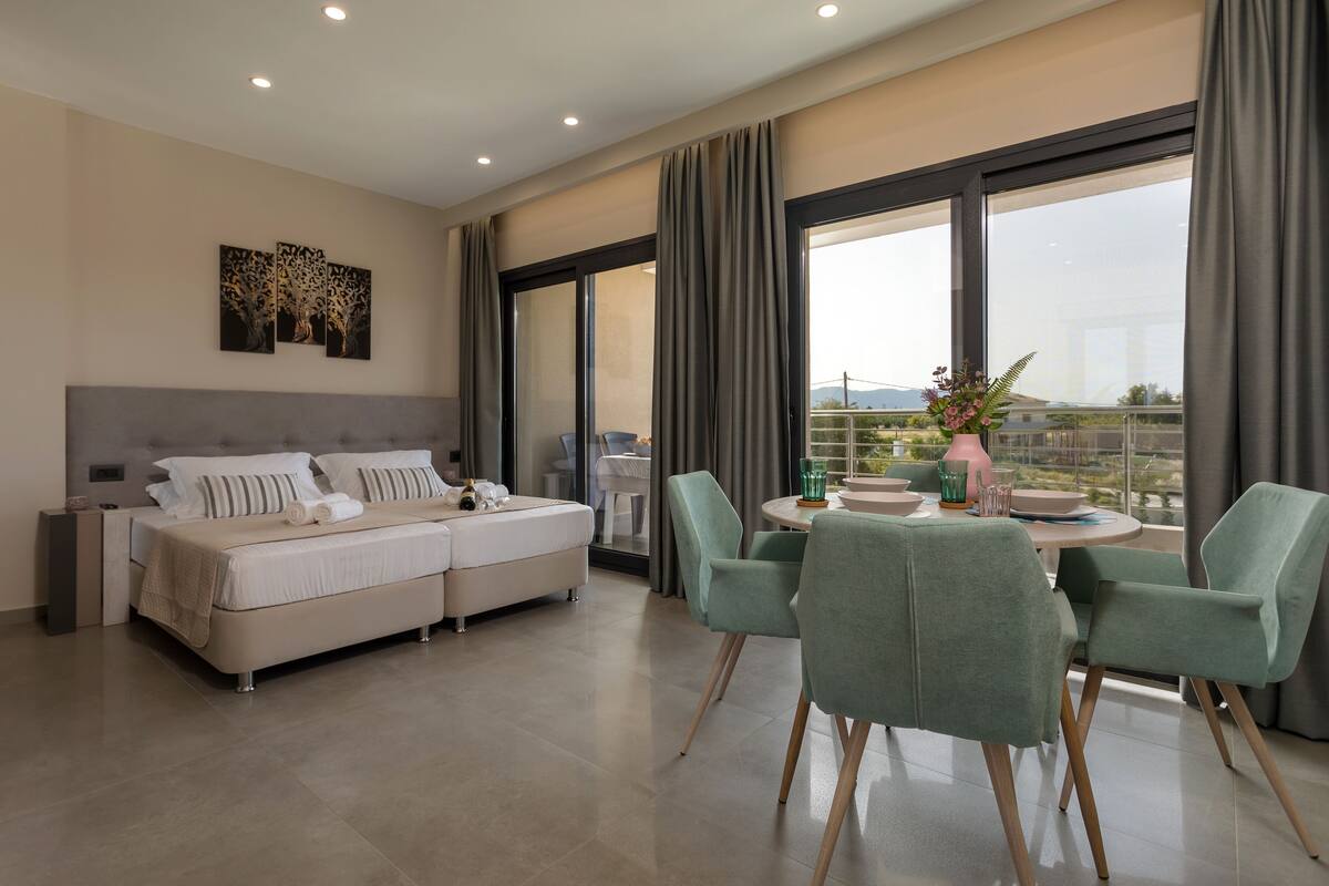 A modern bedroom with a large bed, a dining area with chairs, and a balcony with a view.