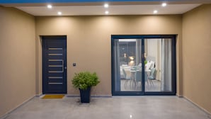 A modern entrance with a dark door, a potted plant, and a glass door leading to a dining area with chairs and a table. - La Casa De Zante (Zakynthos)