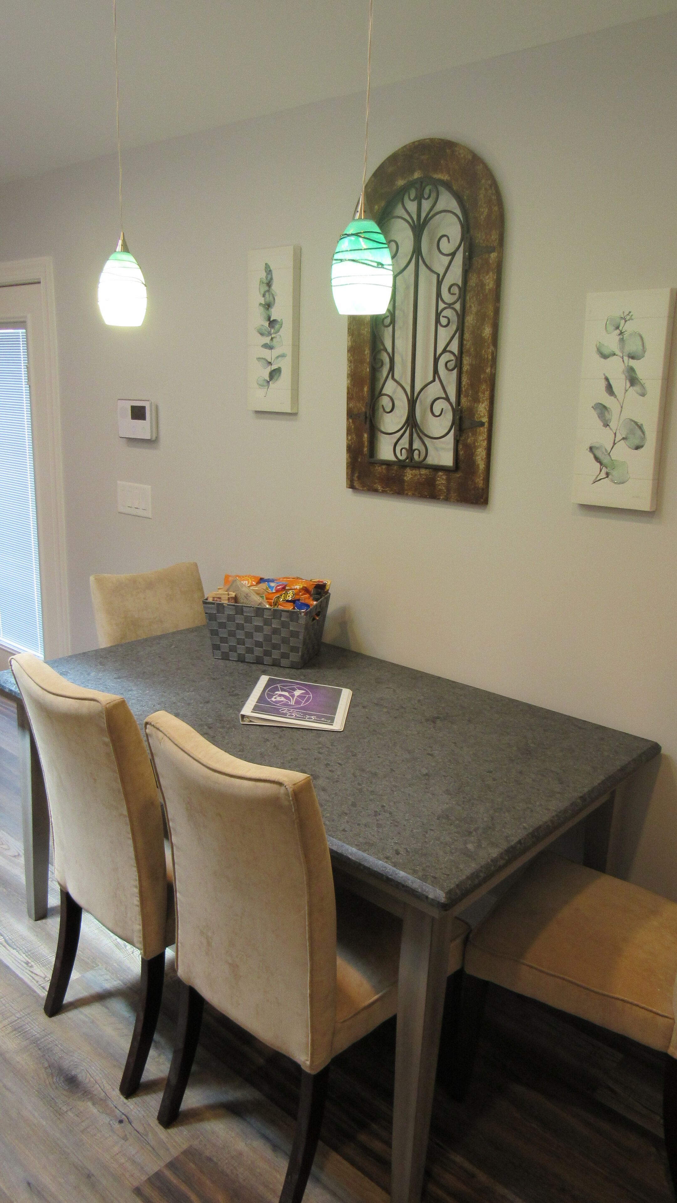 A dining area with a grey table, four beige chairs, a checkered basket with snacks, and two pendant lights.