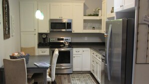 Una cocina moderna con muebles blancos, electrodomésticos de acero inoxidable y un comedor con mesa y sillas.