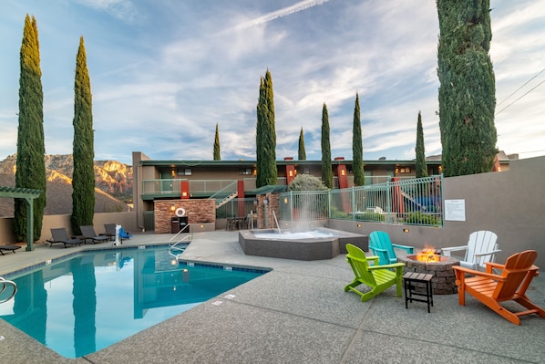Zona de piscina con jacuzzi, asientos al aire libre y altos árboles.