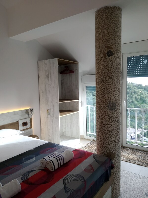 A bedroom with a bed, a wardrobe, a large pillar, and a balcony with a view. - Studio in villa with amazing sea view (Vlorë)