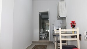 A compact kitchen with a dining area, a small table, and a chair. A white cabinet is above the counter, and a red flower vase is on the wall. - Studio in villa with amazing sea view (Vlorë)