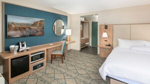 A hotel room with a bed, a desk with a microwave, a coffee maker, a chair, a mirror, and a painting on the wall. - Uptown King Dog Friendly w/ Private Patio  and  Mountain View @ The Matterhorn Inn (Sedona)