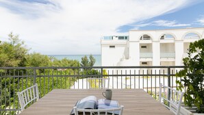 A balcony with a wooden table, a chair, and a white railing overlooking a body of water and a white building with arched windows. - Rivazzurra Homes - 37 (Termoli)