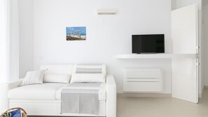 Un salon minimaliste avec un canapé blanc, un téléviseur à écran plat et un climatiseur fixé au mur.