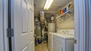 Ein Waschraum mit Warmwasserbereiter, Waschmaschinen und Regalen voller Reinigungsmittel.