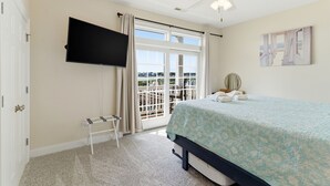 Ein Schlafzimmer mit einem Bett, einem an der Wand montierten Fernseher, einem Deckenventilator und Blick durch das Fenster.