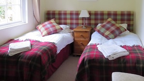 A bedroom with two beds, a nightstand, a lamp, a framed picture on the wall, and a window with curtains. - 2 bedroom accommodation in Duns (Duns)