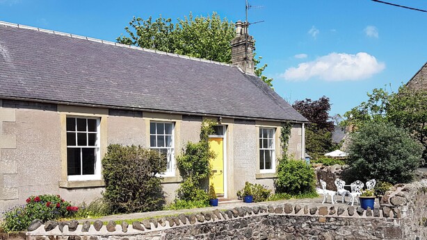 A stone house with a yellow door, a stone wall, and a garden with potted plants and outdoor furniture. - 2 bedroom accommodation in Duns (Duns)