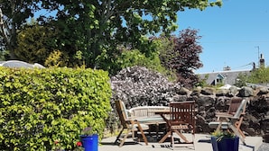 A patio with wooden furniture, potted plants, and a stone wall. - 2 bedroom accommodation in Duns (Duns)