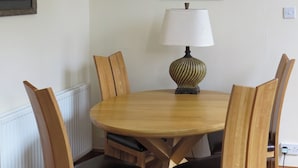 A round wooden dining table with a lamp, four wooden chairs, and framed artwork on the wall. - 2 bedroom accommodation in Duns (Duns)