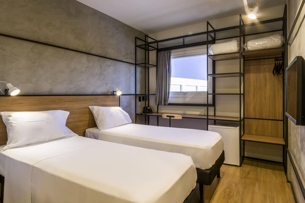 Una habitación de hotel con dos camas, un escritorio, un armario y una ventana con vistas.