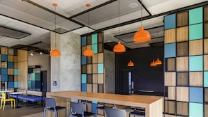 A modern bar area with a long wooden counter, multiple bar stools, and orange pendant lighting. - Ibis Ribeirao Preto Vila do Golf Hotel (Ribeirão Preto)