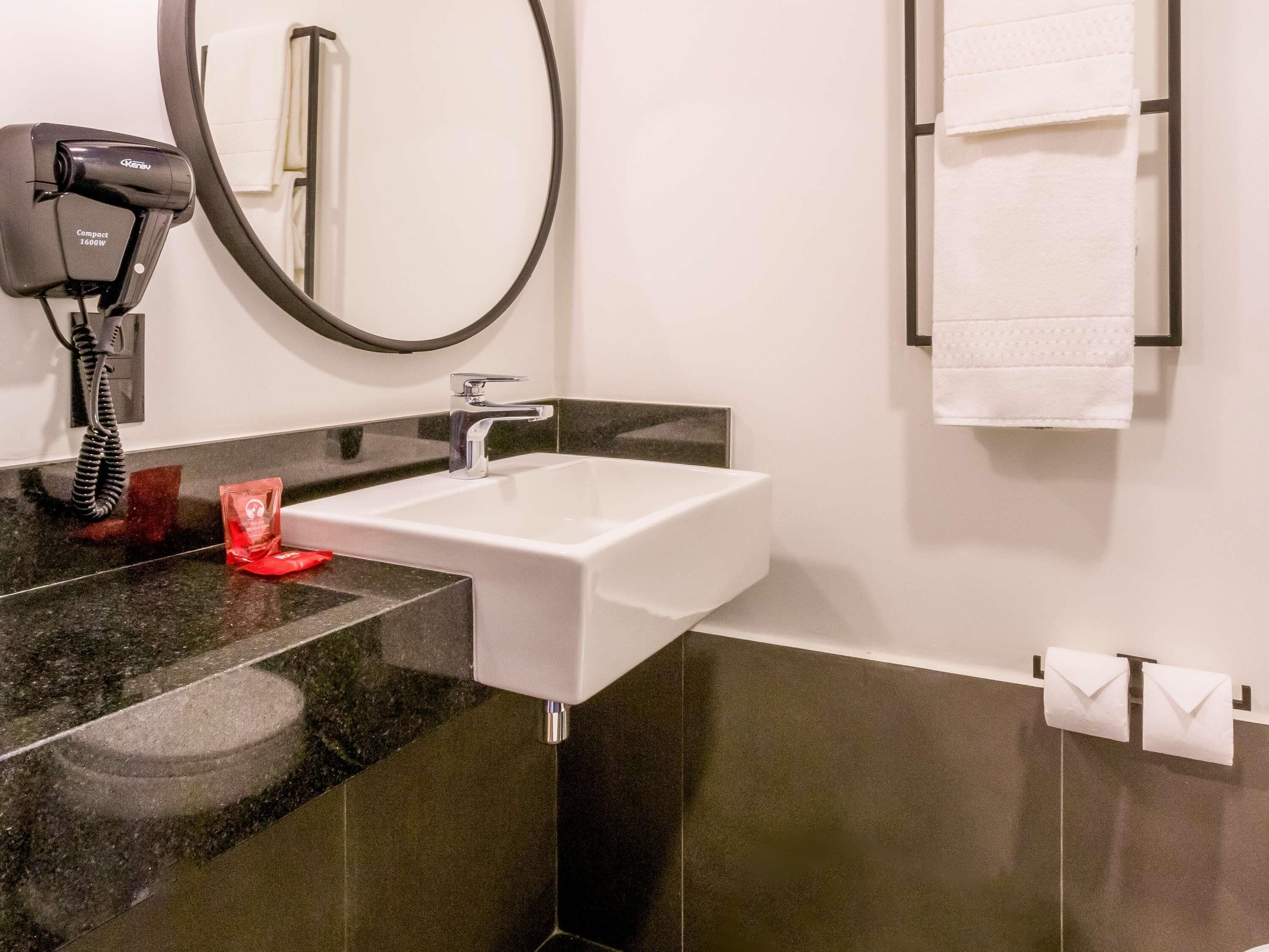 A bathroom with a white sink, black countertop, and a round mirror.