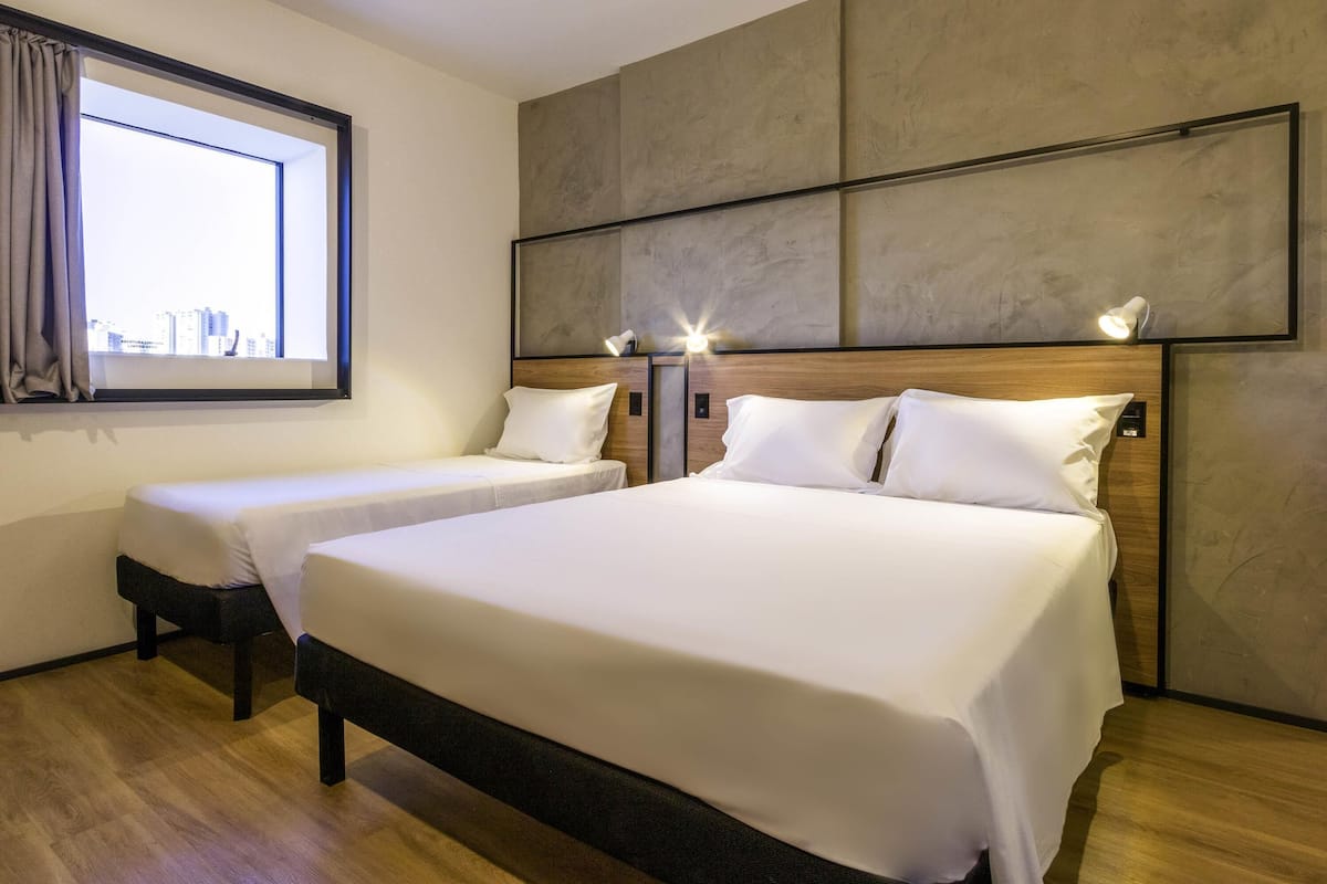 Habitación de hotel con dos camas, un ventanal grande y vistas a la ciudad.