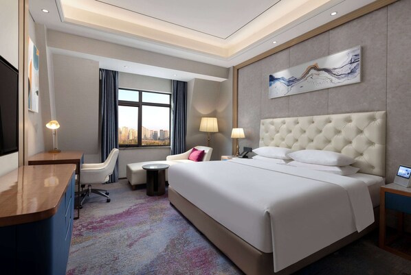 Habitación de hotel con una cama grande, un escritorio, una silla, una mesita y un televisor.
