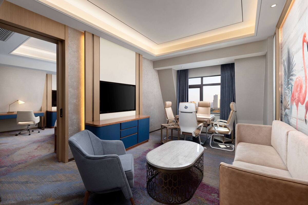 A modern hotel room with a flat-screen TV, comfortable seating, a desk, and a large window.