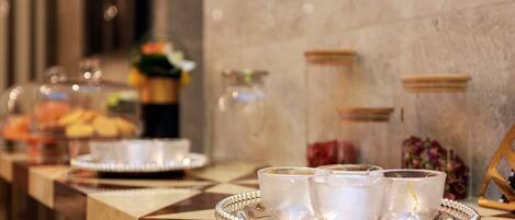 A buffet setup with clear glass cups on a tray, a fruit display, and decorative jars on the wall.