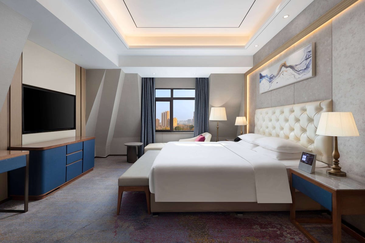 A hotel room with a large bed, a TV, a desk, and a view of the city.