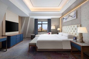 A hotel room with a large bed, a TV, a desk, and a view of the city. - Ramada by Wyndham Zhumadian West Station (Zhumadian)