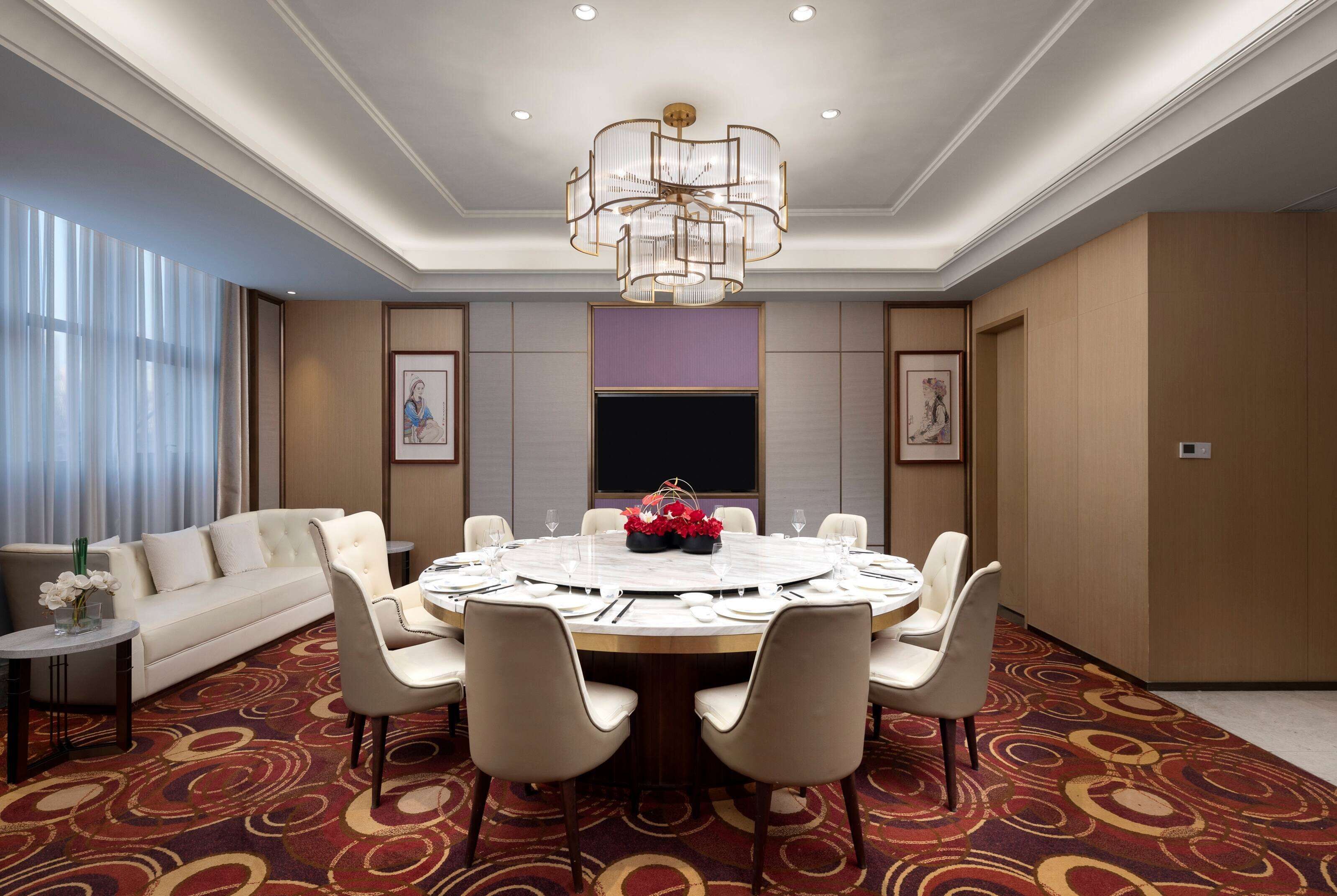 Een vergaderzaal met een ronde tafel, witte stoelen, een kroonluchter en een bank.