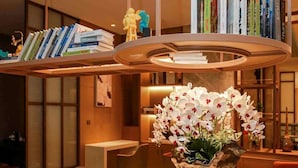 Un interior moderno con una mesa redonda, un jarrón ornamental con orquídeas y una estantería con libros y figuritas.