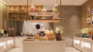 Un moderno vestíbulo de hotel con un mostrador de recepción central, un chef y diversas exhibiciones de comida.