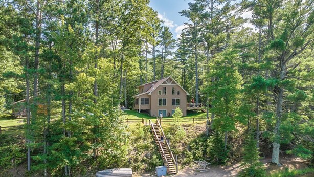A cabin surrounded by dense forest, with a dock and kayaks by a calm lake. - Beautiful Lakeside Home (Woodruff)