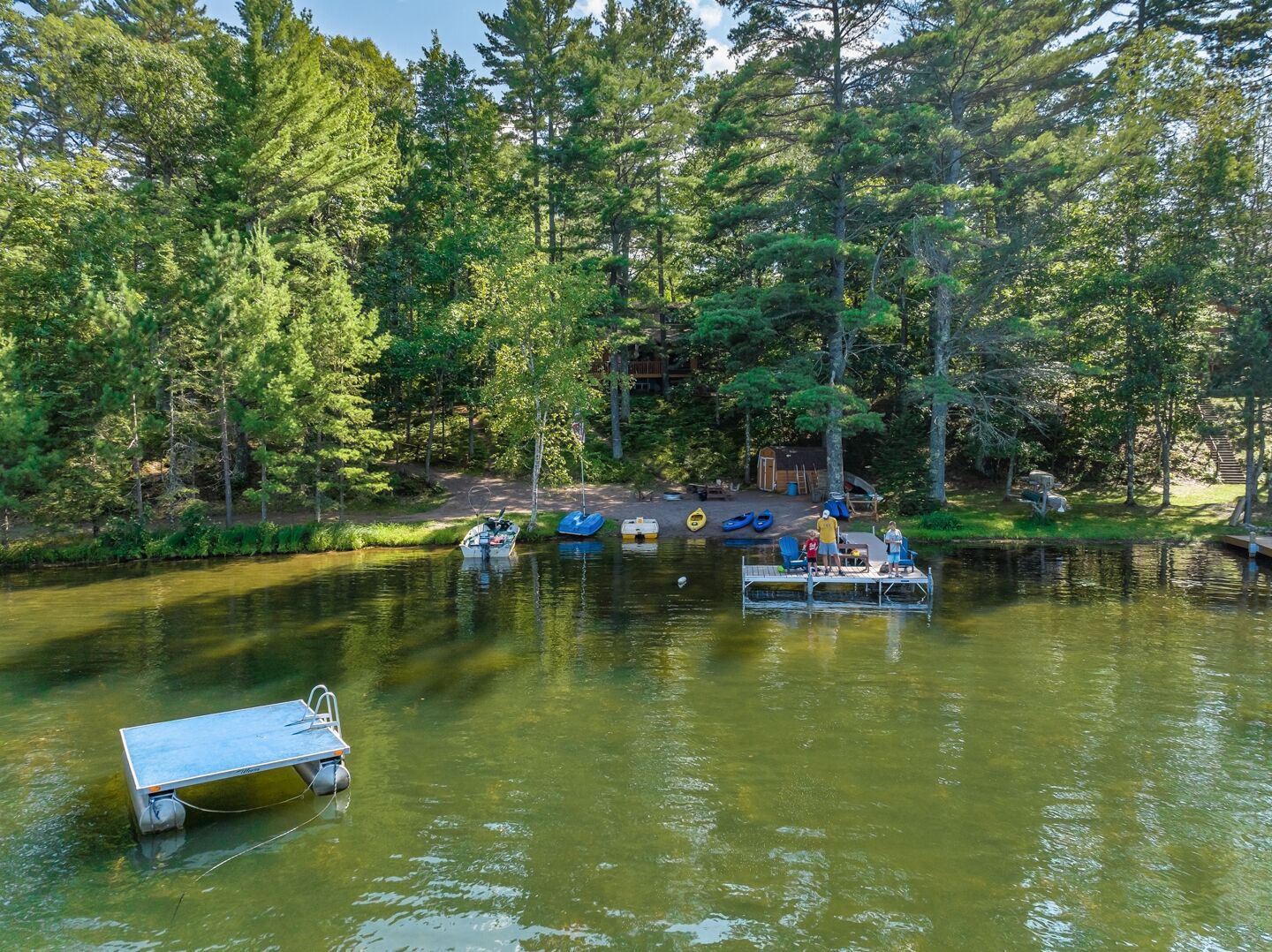 A calm lake surrounded by dense forest, with several boats docked on a wooden pier.