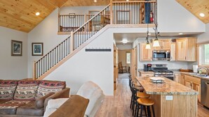 A spacious living area with a wooden ceiling, a staircase leading to an upper level, a kitchen with modern appliances, and a cozy seating area with patterned cushions. - Beautiful Lakeside Home (Woodruff)