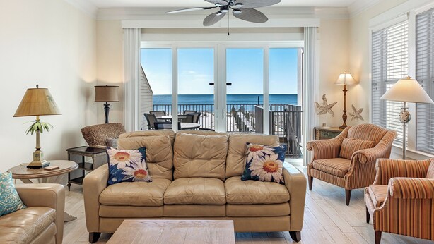 A spacious living room with a beige leather sofa, striped armchairs, and a ceiling fan. Large windows offer a view of the ocean. - 🥰 Summer 2026 Going Fast! 😎 Pearl, West. Huge, beautiful! Heatable Pool. Elevator. Upgrades! (Gulf Shores)