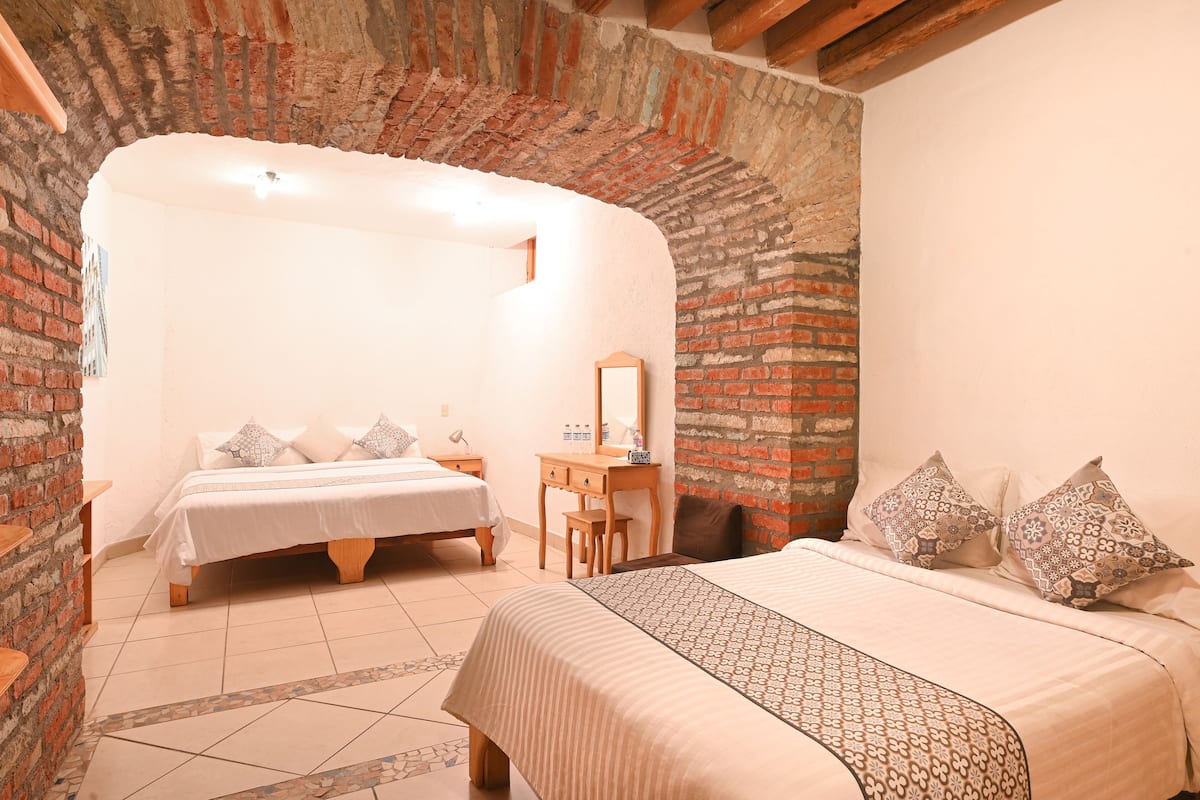 Une chambre avec deux lits, une commode en bois et un mur en briques.