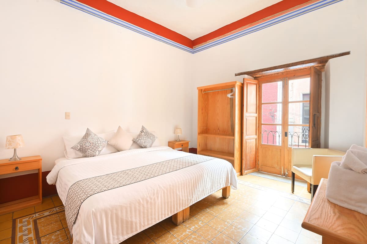 Une chambre à coucher comprenant un lit, des tables de chevet, une armoire en bois, une chaise et une fenêtre donnant sur l’extérieur.